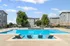 Inviting outdoor pool area with stylish lounge chairs, surrounded by modern three-story apartment buildings and lush greenery.