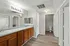 Modern bathroom with dual sinks, sleek gray countertops, and ample storage space beneath. Features bright lighting and a separate toilet area with elegant wood flooring.