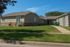 Charming single-story home with classic brick accents, lush green lawn, and inviting entrance under a clear blue sky.