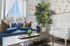 Inviting living room with a plush blue sofa, elegant white armchair, and vibrant potted plant, bathed in natural light.