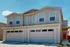 Charming duplex with modern design, featuring two spacious garages and stylish red entryway under a clear blue sky.