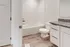 Sleek and modern bathroom featuring a pristine bathtub, elegant vanity with granite countertop, and stylish wood flooring.
