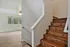 Bright and airy interior with elegant wooden staircase leading to a sunlit space, featuring a large window with serene views.