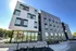 Modern apartment building with sleek design and large windows, featuring a vibrant exterior garden and convenient street access.