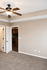 Inviting bedroom with plush carpeting, elegant ceiling fan, and soft neutral tones opening to a cozy kitchen area.