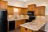 Inviting kitchen with warm wood cabinetry, modern black appliances, and expansive marble countertops, offering a blend of style and functionality.