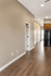 Modern apartment interior featuring a sleek hallway with elegant wooden flooring and bright recessed lighting leading to a kitchen with classic cabinetry.