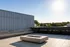Elegant rooftop terrace with modern seating and a sleek stone fire pit, offering a serene view of green landscapes.
