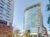 Modern high-rise apartment building with sleek glass exterior and multiple balconies, prime urban location under clear blue skies.