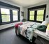 Bright and airy bedroom with large windows, offering a refreshing view of lush greenery, furnished with a cozy bed and modern decor.