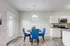 Modern dining area with elegant blue chairs and a round table, adjacent to a sleek kitchen featuring stainless steel appliances and granite countertops.
