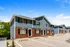 Charming townhouse complex with blue siding and brick foundation, featuring spacious parking and lush greenery under a bright blue sky.