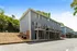 Charming multi-story blue townhomes with private balconies, nestled in a lush green neighborhood under a clear blue sky.