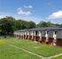 Charming two-story apartments with picturesque green lawns and a serene tree-lined background, under a clear blue sky.