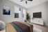 Inviting bedroom with modern decor, stylish bedspread, large windows, and a sleek TV unit on light wood flooring.