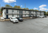 Charming two-story apartment building with modern black-and-white exterior, surrounded by lush greenery and ample parking spaces.