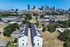Aerial view of contemporary townhouses with sleek white facades, nestled in a vibrant urban landscape with a stunning city skyline in the background.
