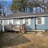 Cozy single-story blue cottage with a wooden deck and white shutters, surrounded by a grassy yard.