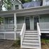 Charming green duplex with inviting front porch and white railing perfect for relaxation.
