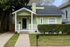 Charming single-story green home with white trim, cozy front porch, and manicured hedges in a friendly neighborhood setting.