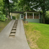 Charming green home with inviting front porch nestled among lush trees, featuring a unique elevated pathway.