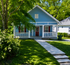 Charming blue cottage with a welcoming porch, lush greenery, and a peaceful suburban setting.