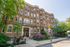 Charming brick apartment building surrounded by lush greenery and vibrant flowers, offering a welcoming residential community vibe.