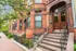 Charming urban apartment building with classic red brick facade, elegant arched entryway, and lush green surroundings.