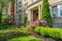 Charming brick apartment building with elegant entrance, framed by vibrant greenery and blooming pink flowers.