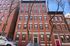 Charming red-brick apartment building with classic architecture and large windows, nestled in a vibrant neighborhood street.