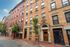 Charming urban apartment building with classic brick facade, arched doorways, and quaint tree-lined sidewalk, epitomizing city living.