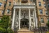 Elegant apartment entrance with grand columns, historic architecture, and beautifully landscaped surroundings.
