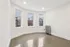 Bright and spacious room with elegant hardwood floors and three large windows offering a scenic city view, perfect for a cozy and inviting living space.