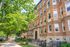 Charming brick apartment building with lush green trees and a welcoming sidewalk in a vibrant neighborhood.