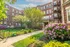 Charming brick apartment building with lush landscaping, vibrant flowers, and a welcoming pathway in a serene setting.