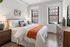 Bright and modern bedroom featuring a cozy bed with vibrant orange accents and large windows welcoming natural light.