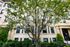 Charming apartment exterior with elegant architecture, nestled behind lush greenery and a picturesque tree.