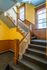 Charming staircase with elegant wooden railings and vibrant yellow walls, illuminated by natural light from large windows.