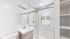 Bright and modern bathroom featuring an elegant glass shower enclosure, sleek vanity with ample storage, and a large window offering natural light.
