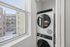 Bright laundry nook with modern stackable washer and dryer, offering a cityscape view from a large window.