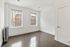 Bright and inviting empty room with polished hardwood floors, two large windows offering urban views, and a classic white radiator, perfect for customization.
