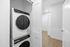 Modern laundry area with sleek stacked washer and dryer, complemented by bright walls and elegant wood flooring.