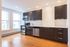 Modern kitchen with sleek dark cabinetry, stainless steel appliances, and elegant hardwood floors, illuminated by natural light from large windows.