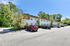 Charming two-story apartment building surrounded by lush greenery with spacious parking, bathed in bright sunshine.