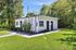Cozy small cottage with a white exterior surrounded by lush greenery and a well-maintained lawn.