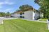 Sunny exterior view of a two-story apartment building surrounded by lush greenery and ample parking space.