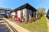 Exterior view of a stylish modern bungalow with vibrant landscaping and a sunny pathway.