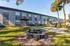 Sunny courtyard with picnic benches and palm trees in front of modern apartment building.