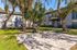 Charming outdoor area with palm trees, a barbecue grill, and a picnic table beside modern apartment buildings.