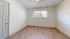 Spacious bedroom with wood flooring, white walls, and a large window with blinds.